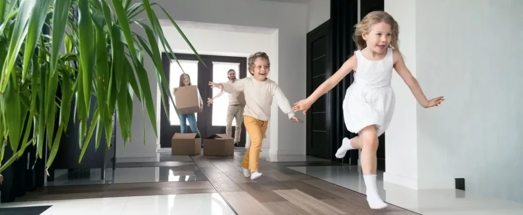 Familie zieht in großes Haus. Kinder rennen durch den Flur, Eltern tragen Kartons
