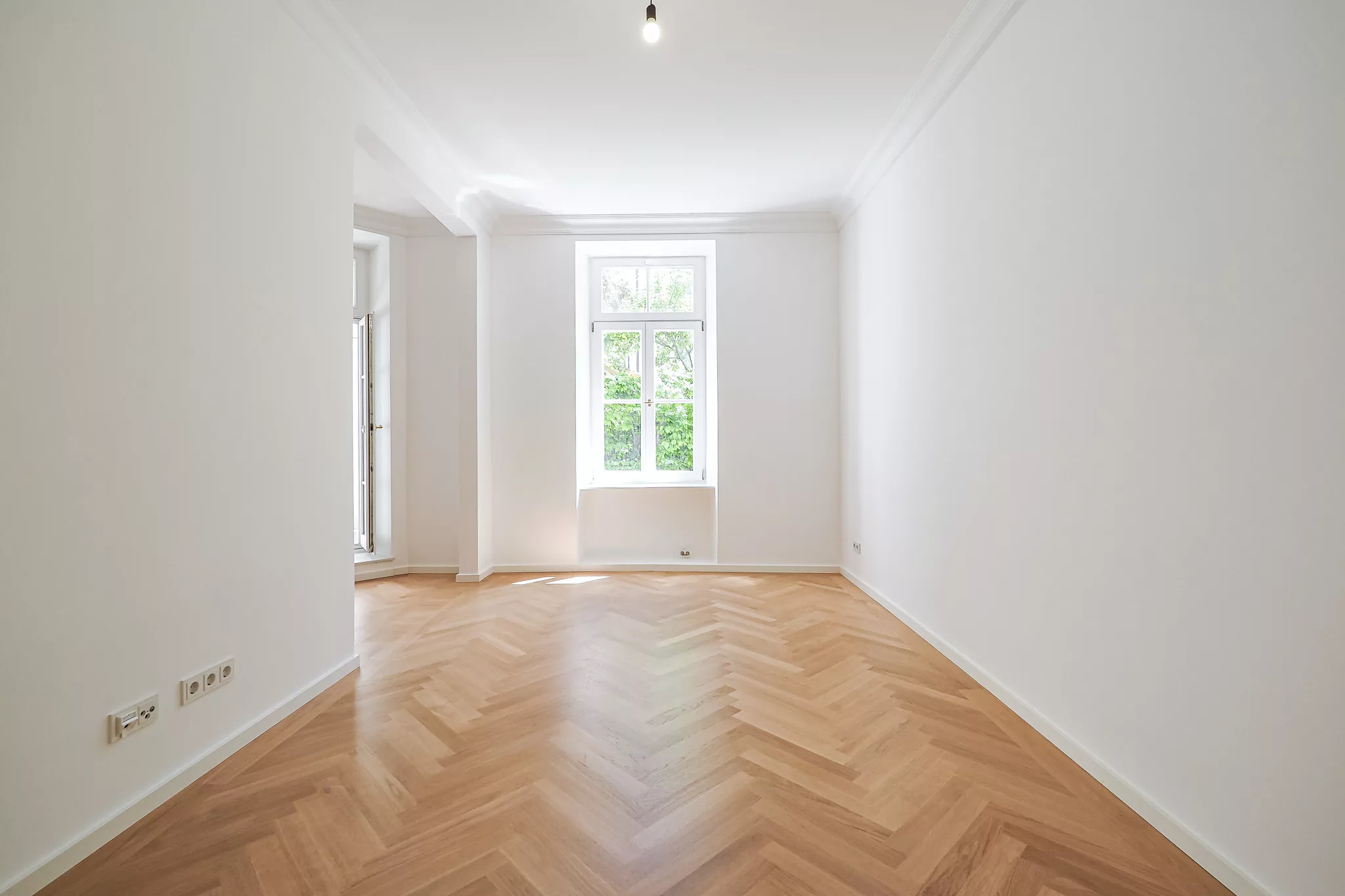 Heller Raum mit Parkettboden und großen Fenstern.