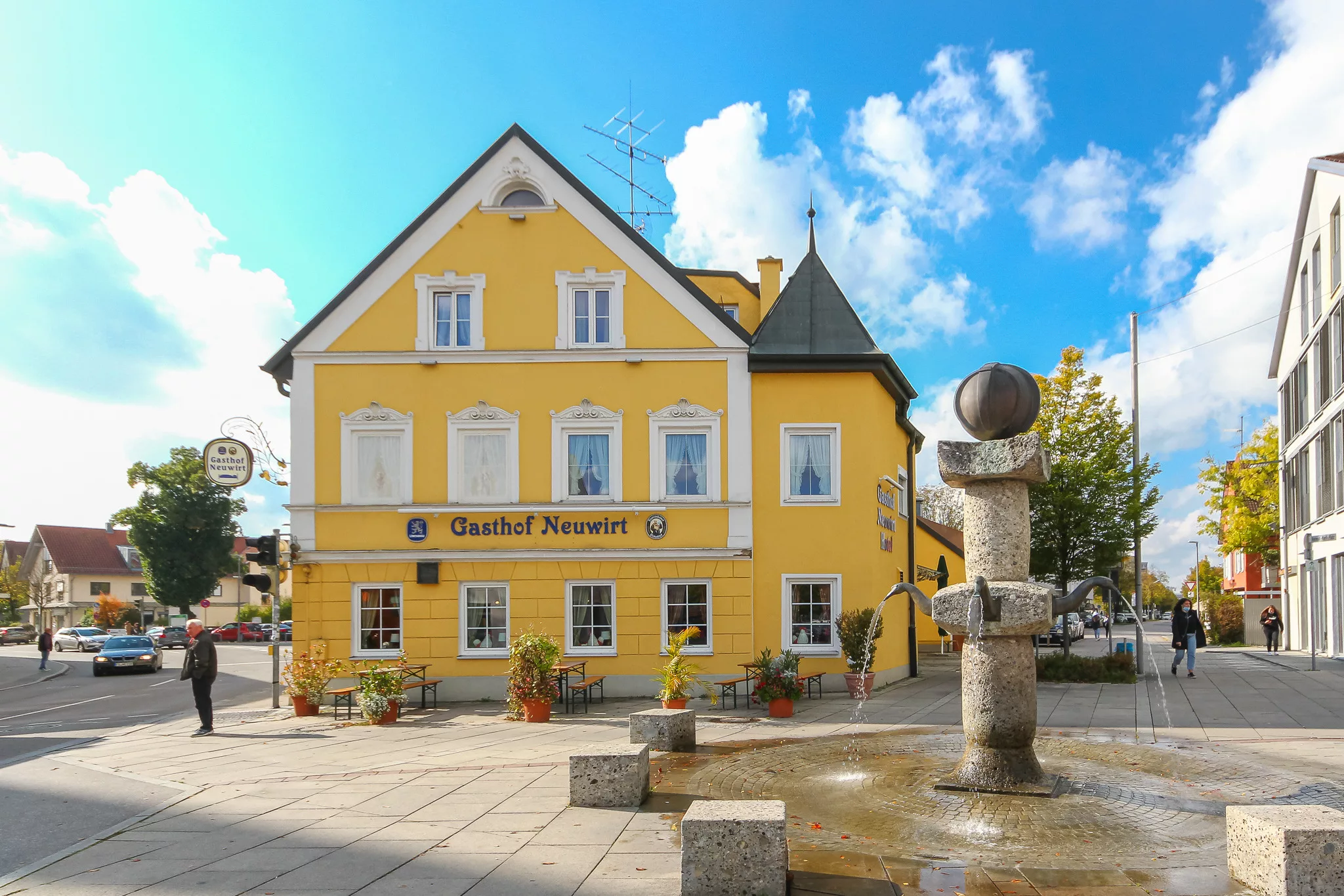 Gelbes Gasthaus mit Brunnen und wolkigem Himmel in Garching