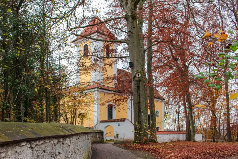 gelbe Kirche mit Bäumen im Herbst in Harlaching