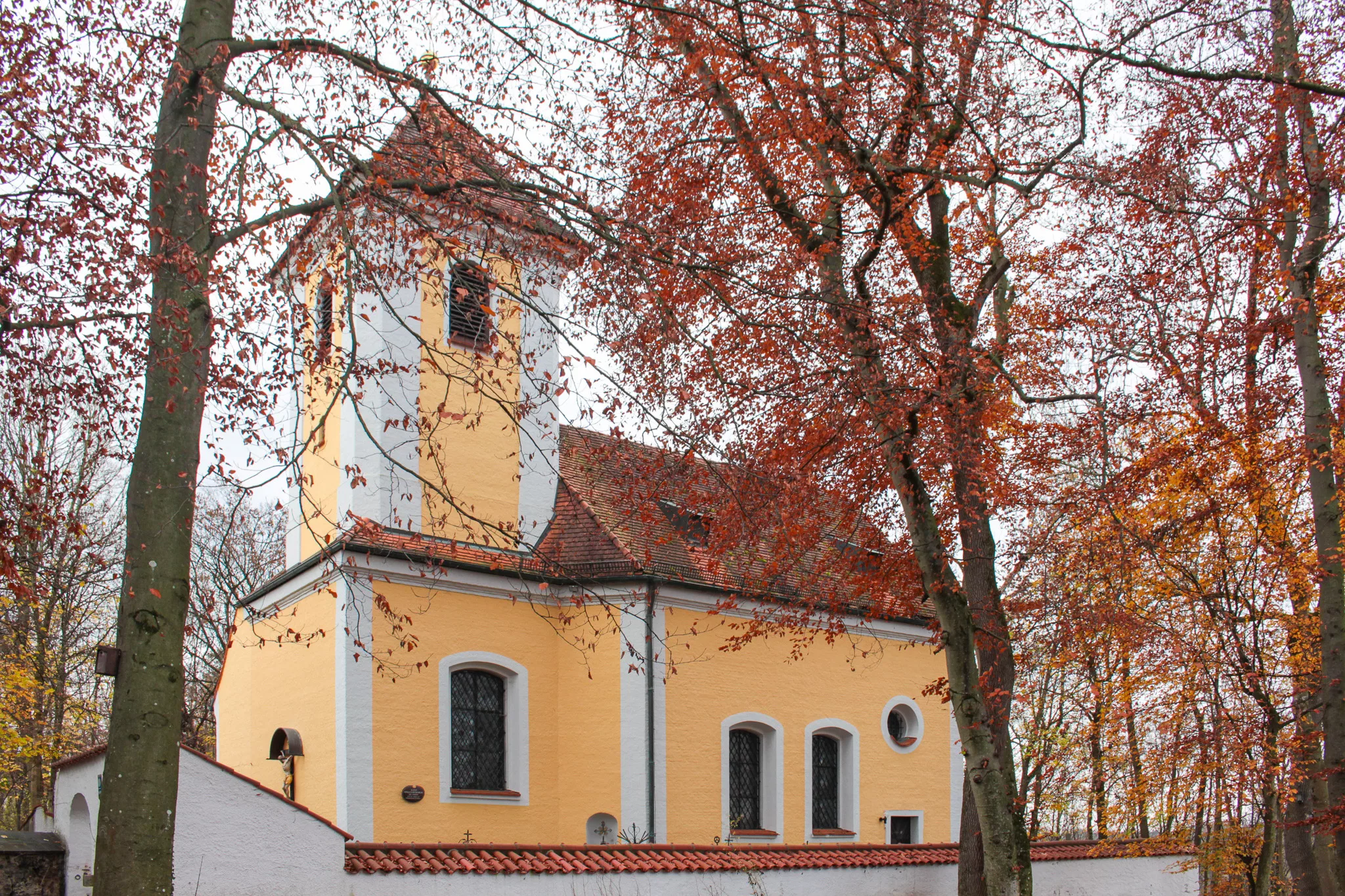 gelbe Kirche mit Bäumen im Herbst in Harlaching