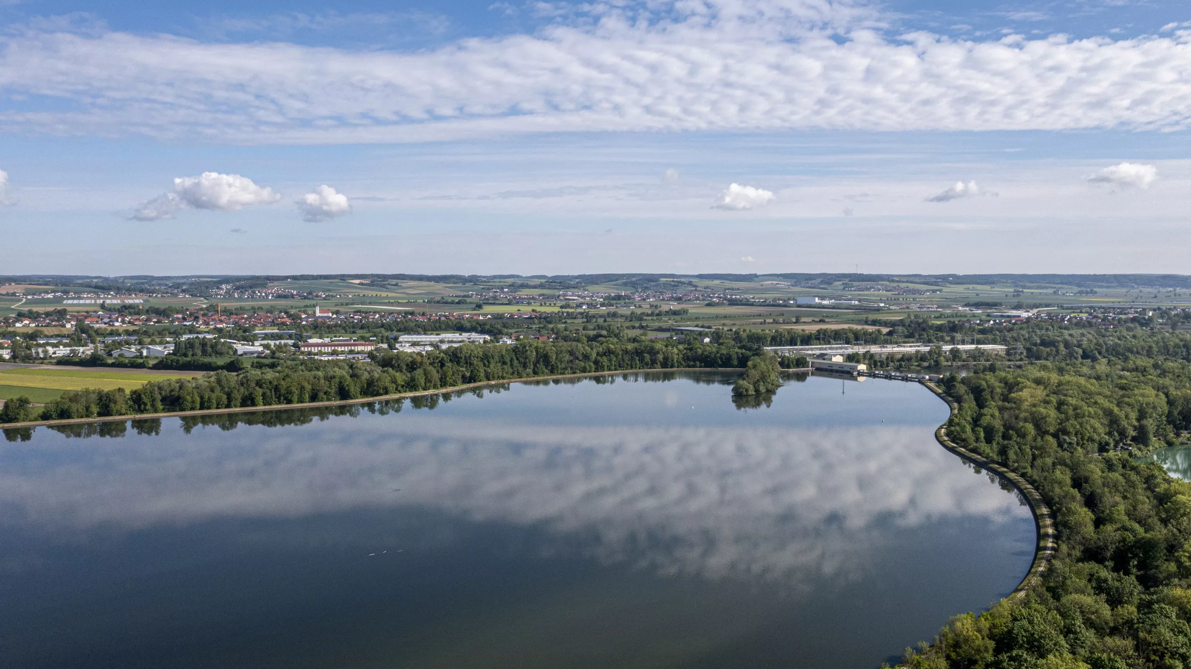 Spiegelndes Wasser mit umliegender Landschaft und Wolken.