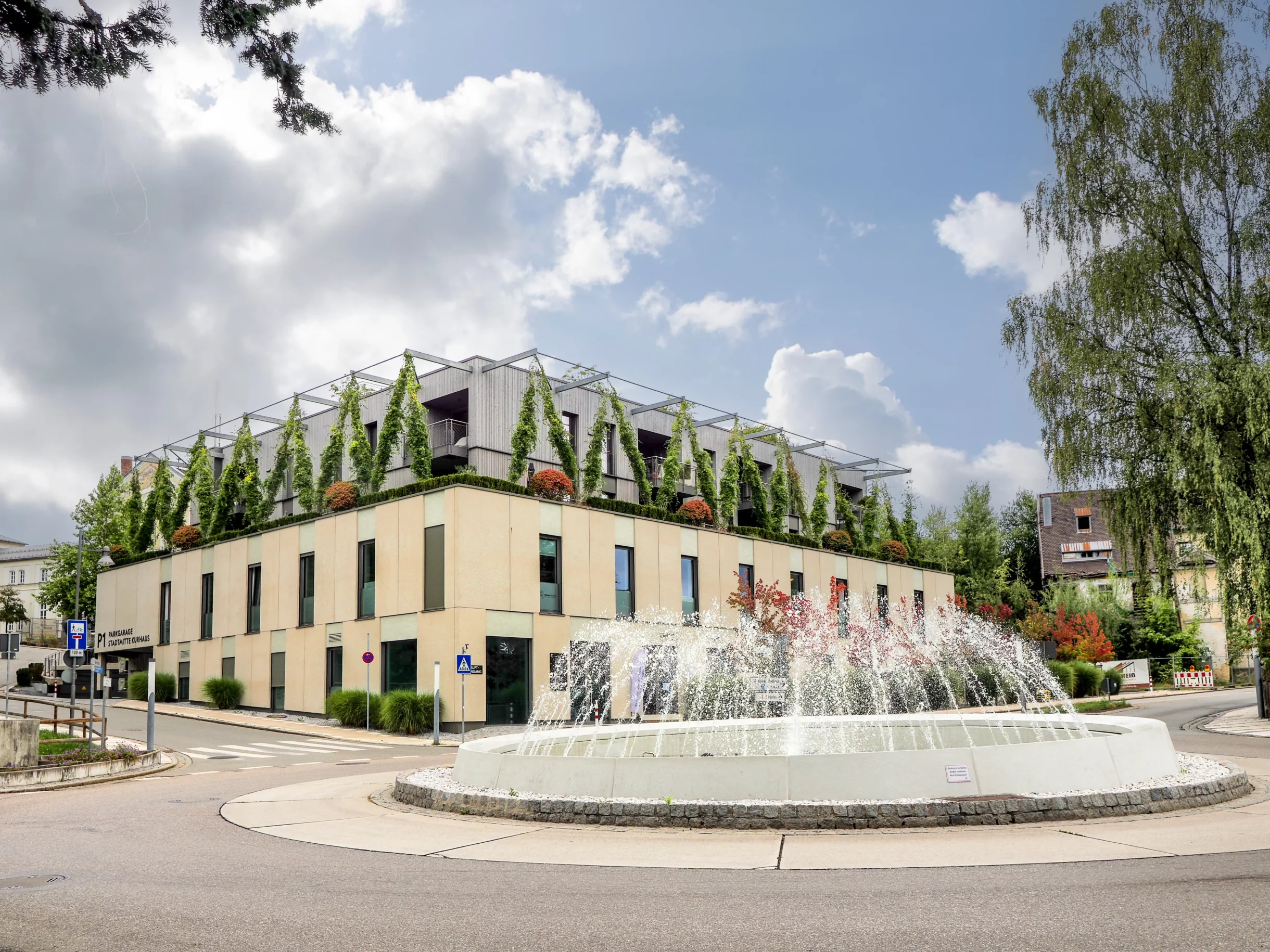 Begrünte Wohnhäuser und Springbrunnen unter blauem Himmel