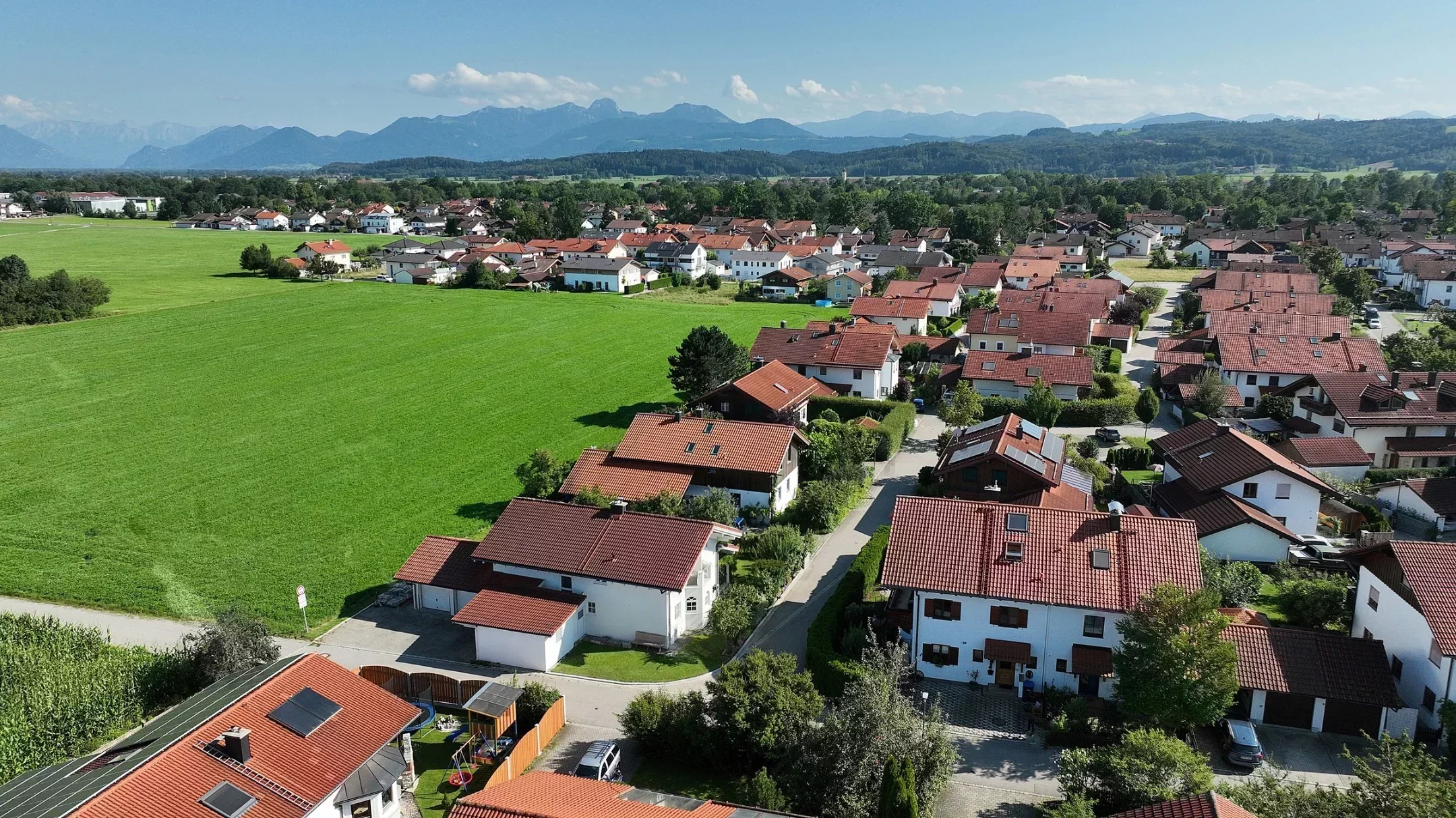 Bayerisches Dorf mit grünen Feldern und Alpenpanorama